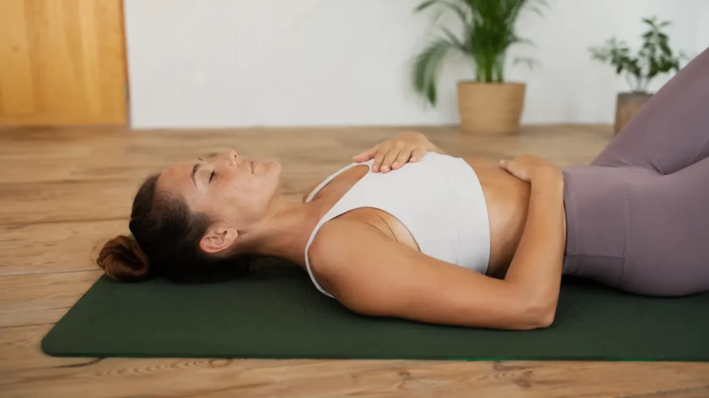 Personne allongée sur un tapis de yoga vert, une main sur le ventre et l’autre sur la poitrine, pratiquant un exercice de respiration.